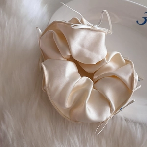 Détail macro du chouchou en satin crème avec de délicats nœuds en ruban et texture soyeuse