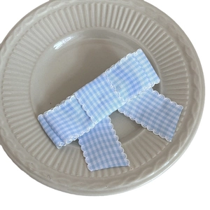 Blue gingham checkered hair clip with white scalloped lace edge on a ceramic plate