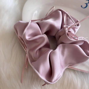 Détail d'un chouchou en satin rose poudré avec petits nœuds sur fausse fourrure blanche