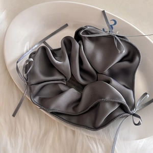 Gros plan d'un chouchou en satin gris foncé avec ruban élégant sur une assiette blanche