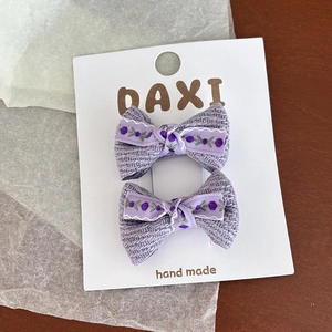 Détail de deux pinces à cheveux en tricot lavande avec ruban floral sur une carte
