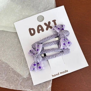 Détails de deux barrettes à nœuds fleuris lavande avec perles sur un fond en bois
