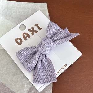 Détail d'une barrette à cheveux en tissu violet avec texture à chevrons sur carton