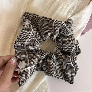 Blue plaid scrunchie hair tie with white flower charm held against a beige background