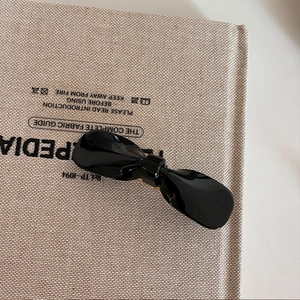 Fermaglio per capelli a fiocco in acetato nero lucido su copertina di libro beige