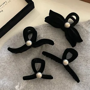 Detailed view of black velvet hair clips featuring silver-grey pearls on soft grey fabric