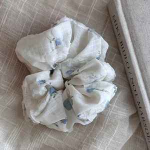 Floral print scrunchie in blue and white fabric displayed on a textured beige tablecloth