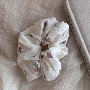 Floral white scrunchie with purple flowers on beige linen next to an art book