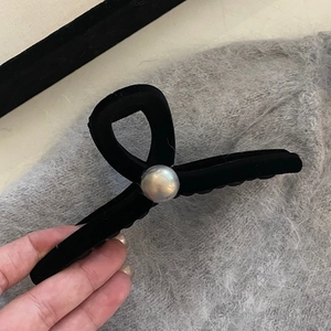 Detail of a black velvet hair claw clip with a large white pearl on a soft background