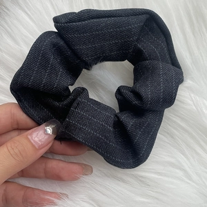 Detail of grey plaid hair scrunchie with white pinstripes shown on hand with fur background