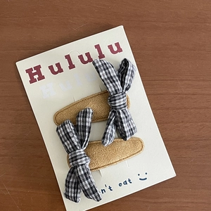 Detailed view of black and white plaid bow hair clips with corduroy texture on white card