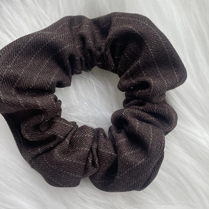 Detail of a brown plaid scrunchie with golden metallic threads on a plush white surface