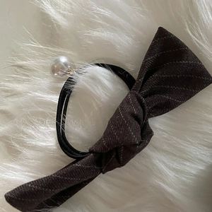 Elegant plaid bow hair tie with polished pearl accent on soft plush white background