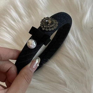 Detail of a black fabric headband featuring a small bow, white pearl, and rhinestone flower