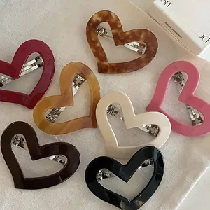 Flat lay of heart-shaped hollow hair clips in multiple colors on beige linen cloth