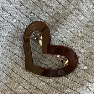 Brown heart-shaped hollow metal hair clip displayed on grey knit fabric texture