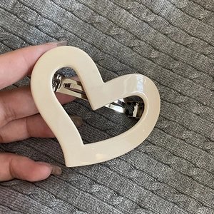 Minimalist cream heart spring hair clip held against a textured grey knitted sweater