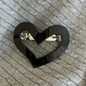 Detail of a glossy black heart-shaped hair clip on a textured grey knit sweater