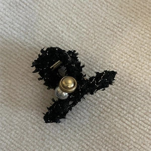 Détail de la pince à cheveux en tweed noir avec bouton doré et perle grise