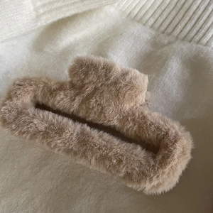 Close-up of a large brown plush hair claw clip with soft faux fur on white knit fabric