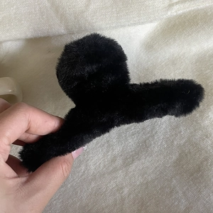 Détail de la texture douce d'une grande pince à cheveux en peluche noire tenue à la main