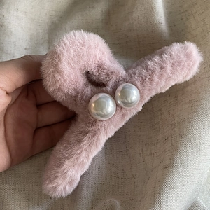 Détail d'une pince à cheveux en peluche rose avec perles sur lin gris texturé