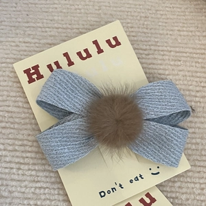 Eleganter Baby-Haarclip mit Schleife und braunem Bommel auf strukturiertem hellblauem Stoff