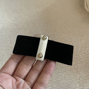 Detail of black velvet hair clip featuring cream center strap and gold metal rivets