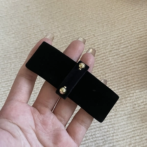 Detail of elegant black velvet hair clip with double gold spheres on a neutral background