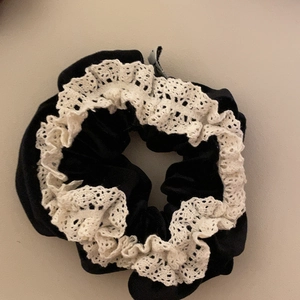 Detailed view of a black velvet hair scrunchie with white lace trim and elastic stretch