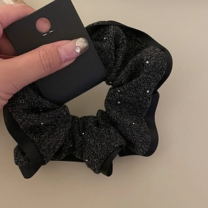 Dettaglio dell'elastico per capelli in tweed nero con paillettes e bordo in raso