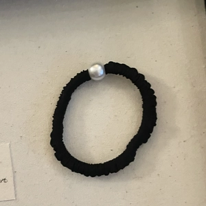 Elastico per capelli nero con perla bianca sintetica su superficie grigia rugosa