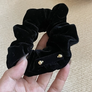 Detail of a black velvet scrunchie featuring decorative gold metallic accents on the fabric
