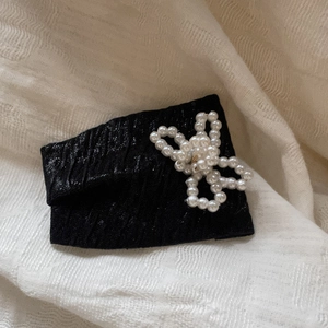 Detail shot of black fabric hair clip featuring elegant white pearl butterfly embellishments