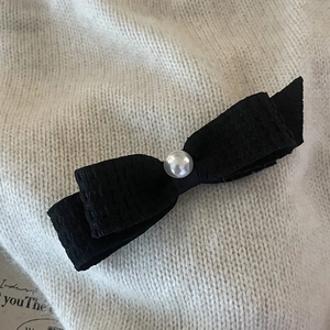 Elegant black fabric bow hair clip with central white pearl on a cream textured background