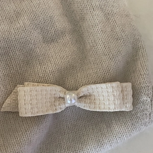 Macro shot of beige tweed bow hair clip with white faux pearl on grey knit fabric