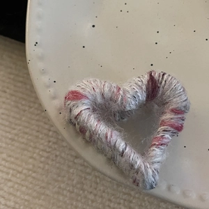 Close-up of heart-shaped knit hair claw clip in pink and grey woven wool texture