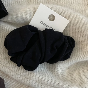 Chouchou en tissu noir minimaliste présenté sur une surface en maille blanche
