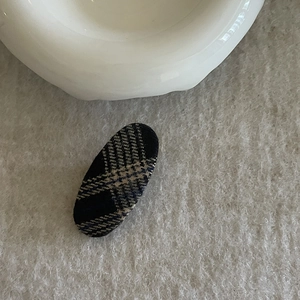 Close-up of vintage blue and beige plaid fabric oval hair clip on textured linen cloth