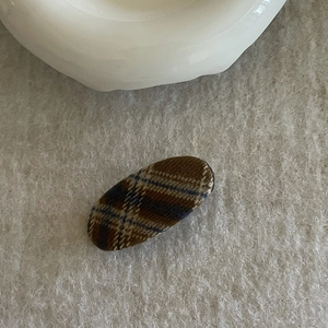 Detailed view of the fabric-covered brown and blue plaid hair clip on felt surface