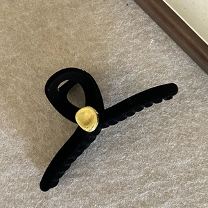 Detail view of large black flocked shark hair claw clip with golden circular accent