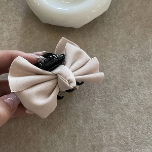 Detailopname van beige wollen strik haarspeld met zwarte plastic clipbevestiging