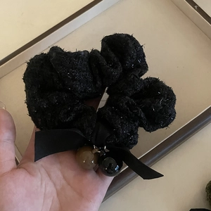 Close-up of black tweed scrunchie featuring a bow ribbon and decorative round bead charms