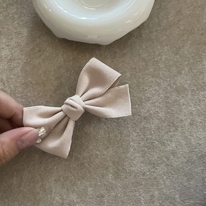 Detailopname van een beige wollen strik haarklem met verfijnde stiksels en zachte textuur