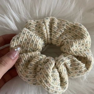 Chouchou en tricot crème avec mouchetures pastel sur un fond de tissu en peluche blanc