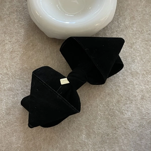 Elegante zwarte fluwelen strik haarclip met gouden accent op beige getextureerde achtergrond