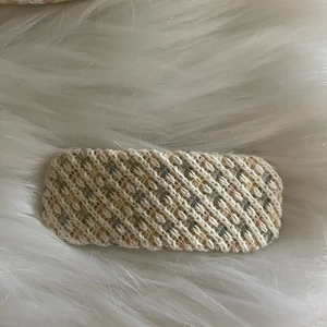 Détail d'une barrette en tricot crème avec fils colorés sur fond en peluche blanc