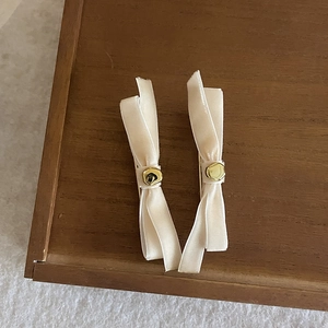 Pair of cream satin bow hair clips with gold metal accents on a wooden tray