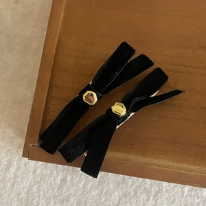 Detail view of two black velvet bow hair clips with gold hexagonal accents on wood background
