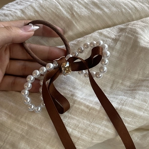 Détail de l'élastique à cheveux en satin marron avec perles et pierre ambre centrale